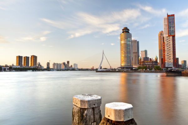View on the river Maas in Rotterdam from the west. In the foreground two bollards. In the background on the right the Southbank Kop van Zuid with a.o. the Montevideo, in the midst Hotel New York and on the left front the World Port Center in addition to the Erasmus Bridge.