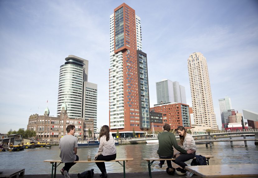 People at the terrace of Fenix Food Factory, with a view on the highrise of the Kop van Zuid, including Hotel New York and the Montevideo building.