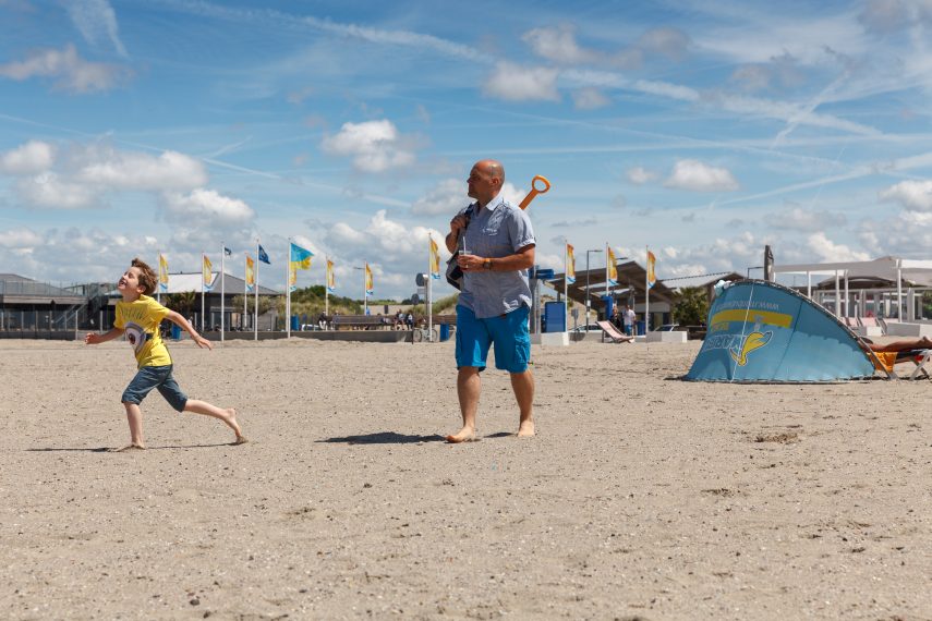 A man and a child walking at Hoek van Holland beach. The boulevard is visible in the background.