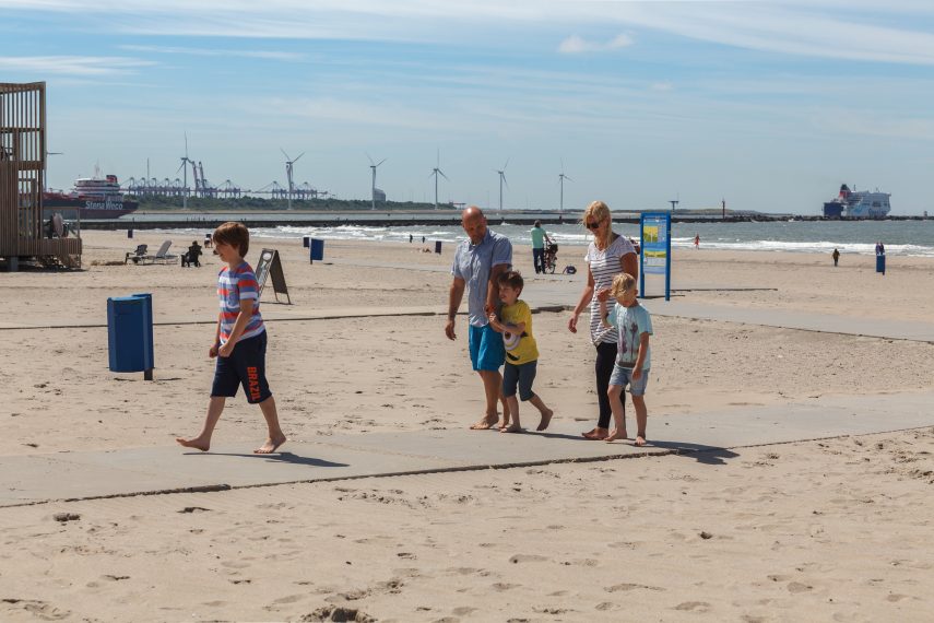A family at Hoek van Holland beach. The pier, wind turbines and a ship at sea are visible in the background.