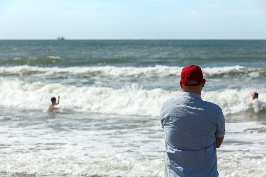 Father looking at children playing in the surf at Hoek van Holland (Hook of Holland) beach.