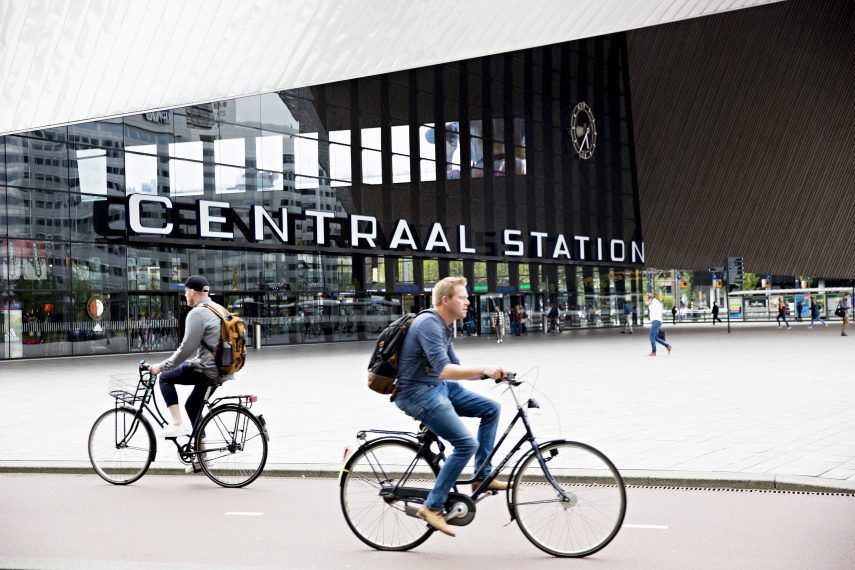 Fietsers rijden voorbij Rotterdam Centraal dat ontworpen is door Benthem Crouwel Architekten.