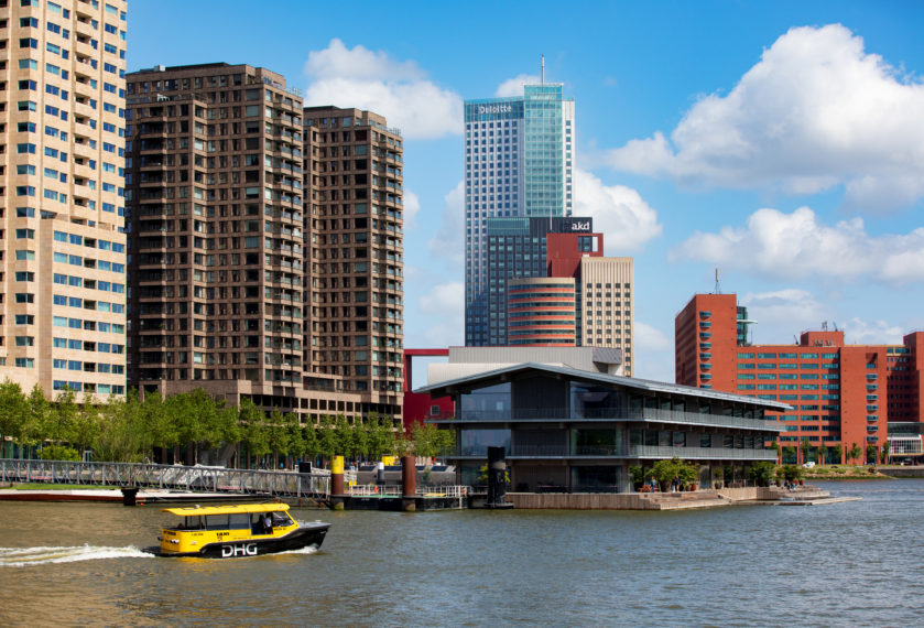 De Rijnhaven met de indrukwekkende hoogbouw en skyline. Het drijvende kantoor (Floating Office) van het GCA op de voorgrond. Een watertaxi vaart voorbij.