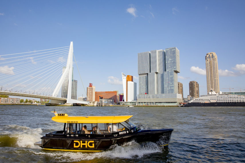 Een watertaxi vaart over de Maas, met zicht op de Erasmusbrug en de Rotterdam.