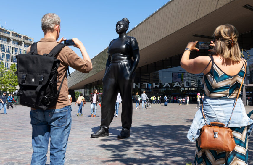 Mensen maken een foto van Moments Contained, het bijna 4 meter hoge bronzen beeld van een jonge, fictieve, gekleurde vrouw op sneakers, handen gebald in de zakken van haar trainingspak. Met een uitstraling van weerbaarheid, zelfvertrouwen en kwetsbaarheid. Het beeld staat op het Stationsplein, direct voor het Centraal Station. De vrouw staat niet op een sokkel, maar met beide voeten op de grond. Het beeld is gemaakt door de Engelse kunstenaar Thomas J Price en is aan de stad Rotterdam geschonken door de Stichting Droom en Daad. Het maakt deel uit van de Internationale Beelden Collectie van Rotterdam. Het beeld werd begin juni 2023 onthuld. 