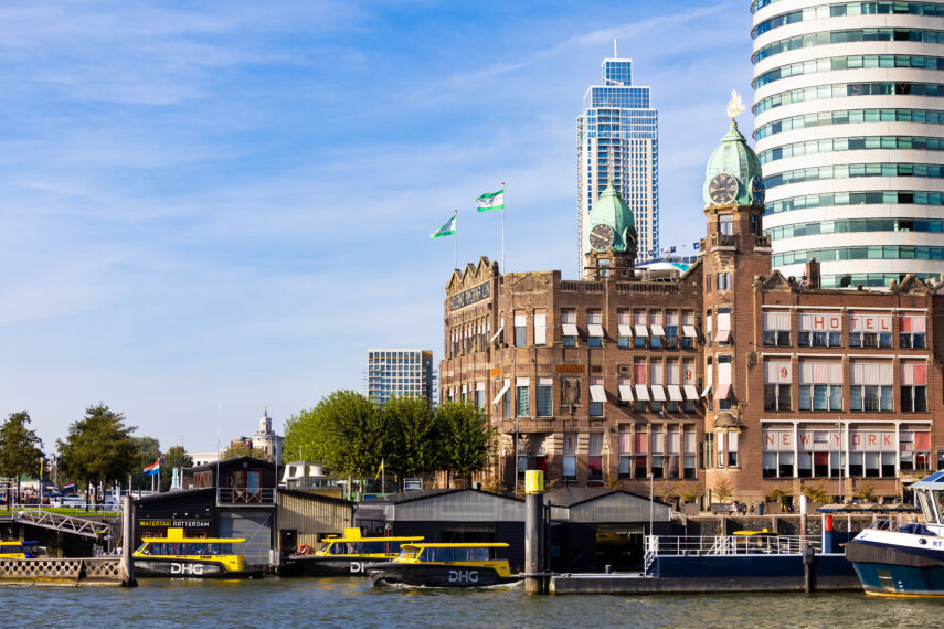 Een foto van enkele architectonische iconen van Rotterdam: Hotel New York, watertaxihalte en op de achtergrond de Zalmhaventoren, het hoogste gebouw van Nederland.