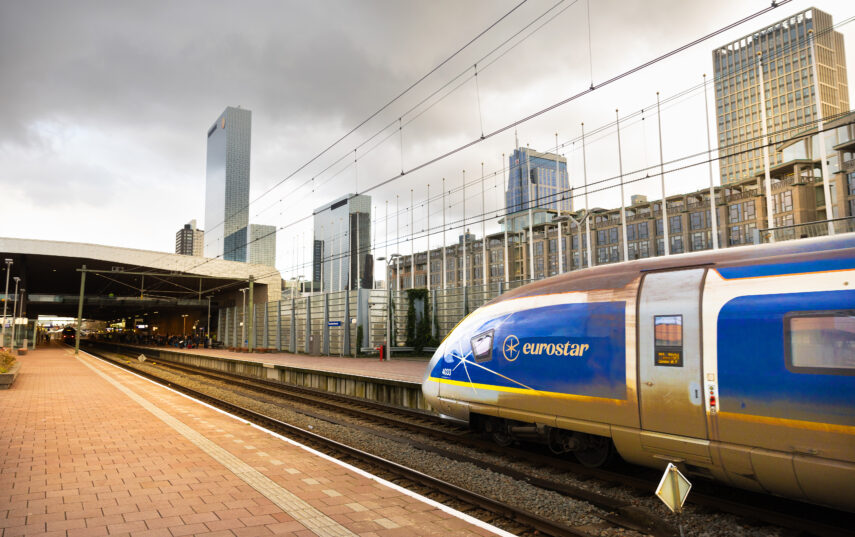 A Eurostar train arrives at Rotterdam Central Station. Part of the skyline is visible in the background, with the Delftse Poort highrise to the left.