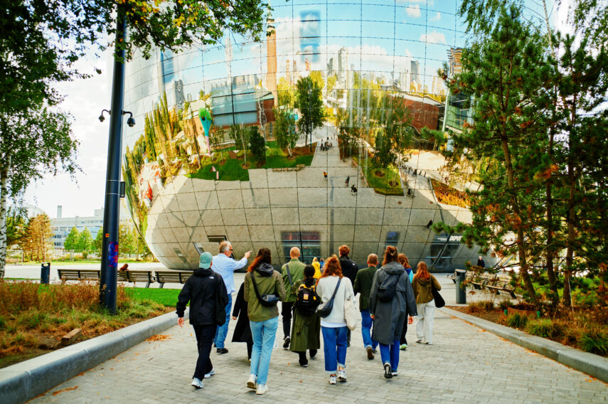 Een groep mensen loopt richting Het Depot van Museum Boijmans Van Beuningen. In de weerspiegeling van Het Depot zie je de stad op de achtergrond. 