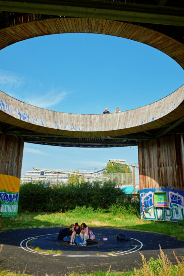 Een groepje meiden zit onder de Luchtsingel, met op de loopbrug twee mensen die genieten van het uitzicht. 
