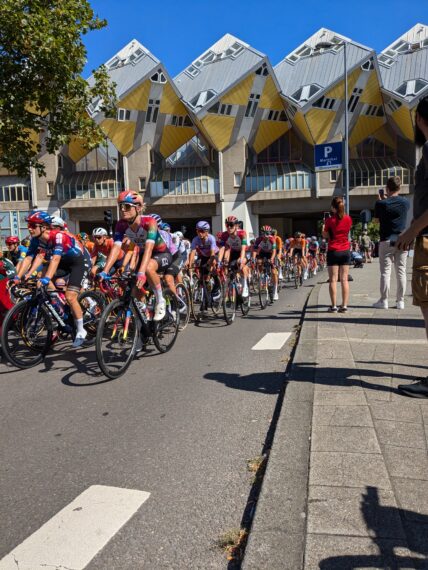 De wielrensters van Tour de Femmes komen onder de gele kubuswoningen vandaan bij de Blaak