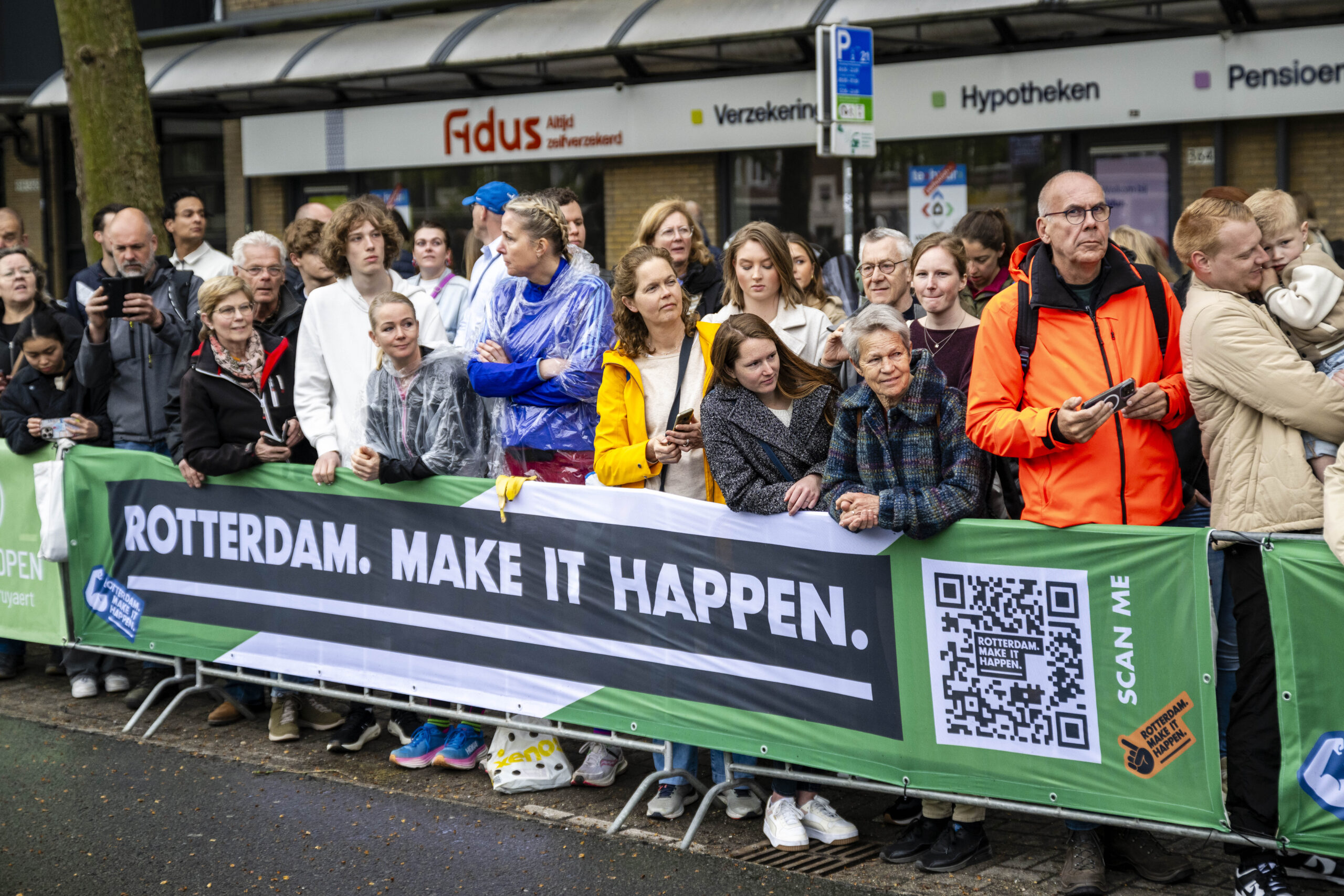 Mensen staan achter een hek met spandoek tijdens een evenement in Rotterdam.
