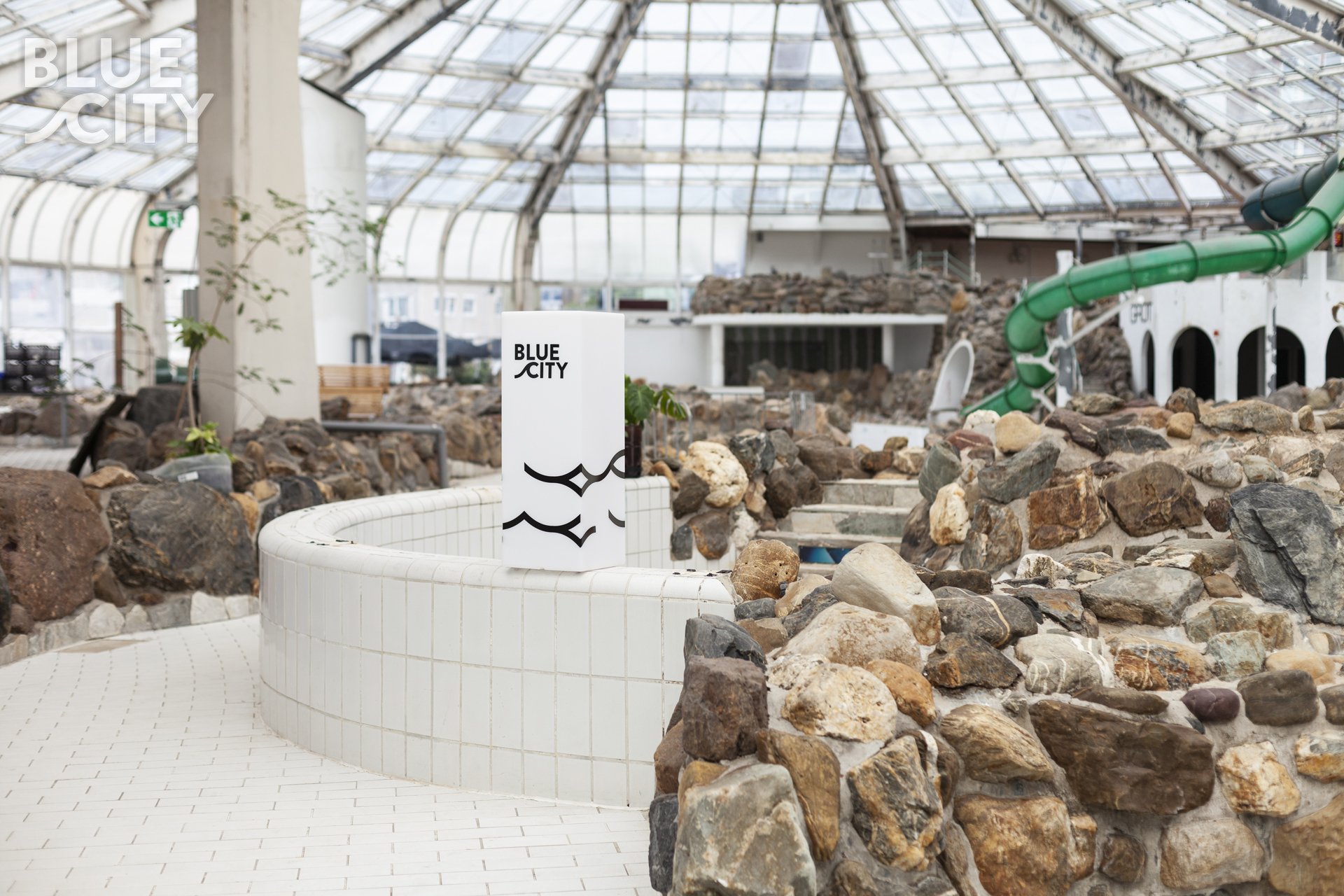 Interieur van BlueCity met glazen dak, stenen muren en groene glijbaan.