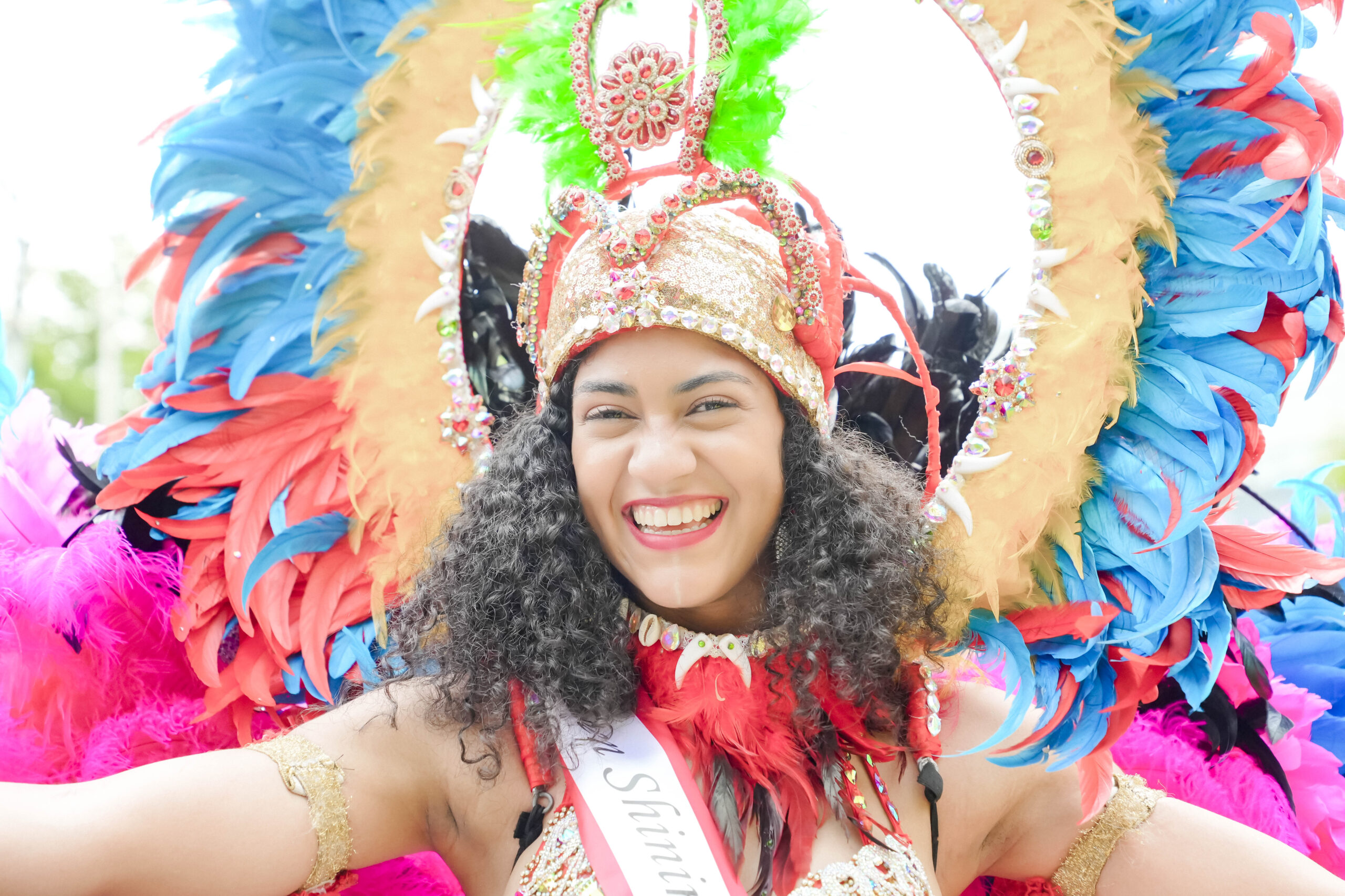 Vrouw in kleurrijke carnavalskostuum met veren en glimlachend gezicht.