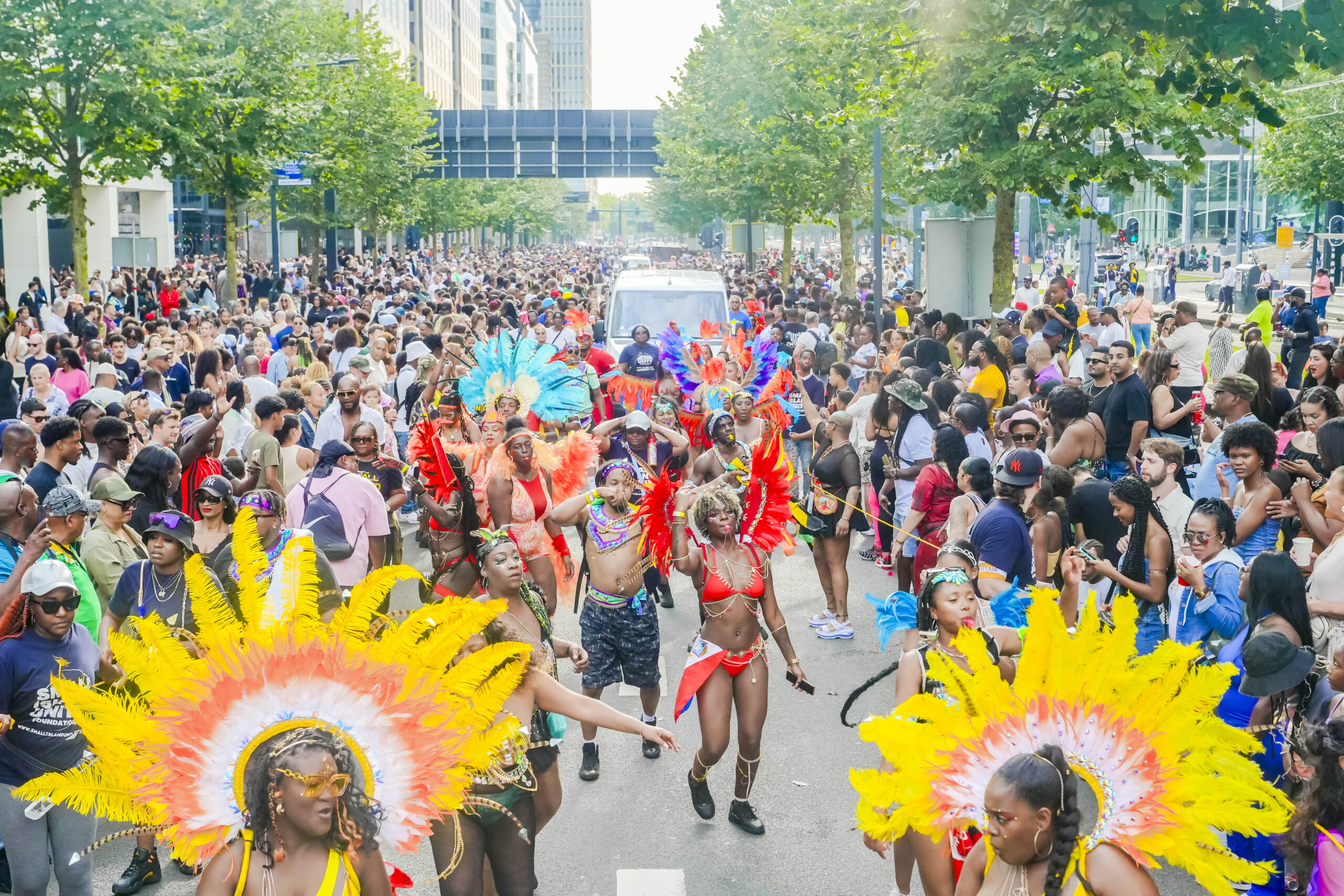 Mensen in kleurrijke kostuums dansen in een drukke parade op straat.