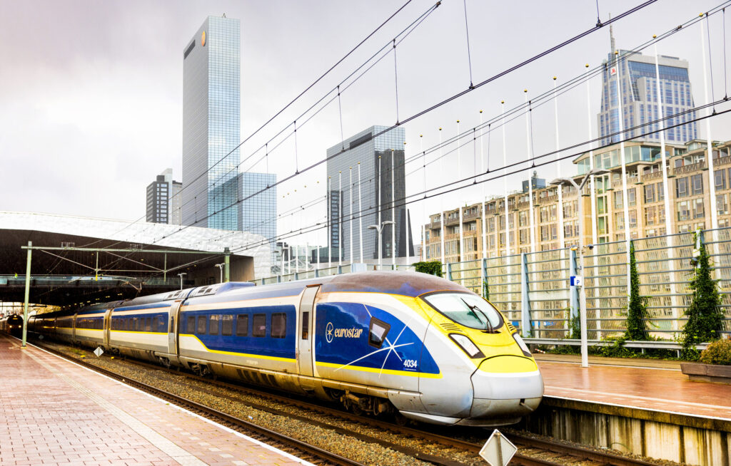 Een Eurostar trein vertrekt vanaf Rotterdam Centraal Station. Een deel van de skyline, met gebouw Delftse Poort, is zichtbaar in de achtergrond.
