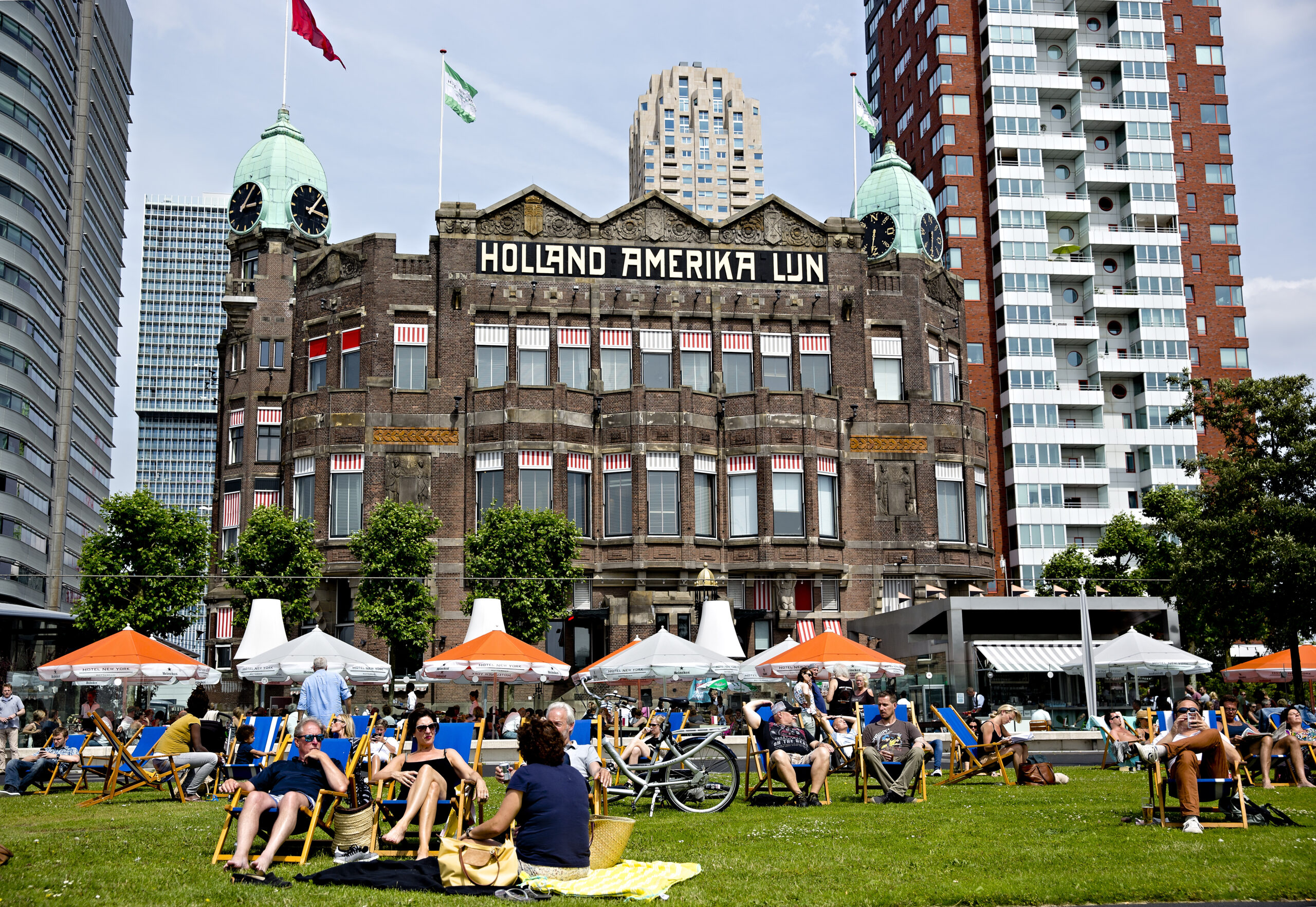 Mensen genieten van de zon op het grasveld voor Hotel New York.