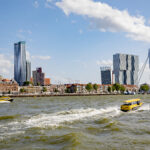 Skyline van Rotterdam vanaf Noord gezien waarop twee watertaxi's voorbij varen.