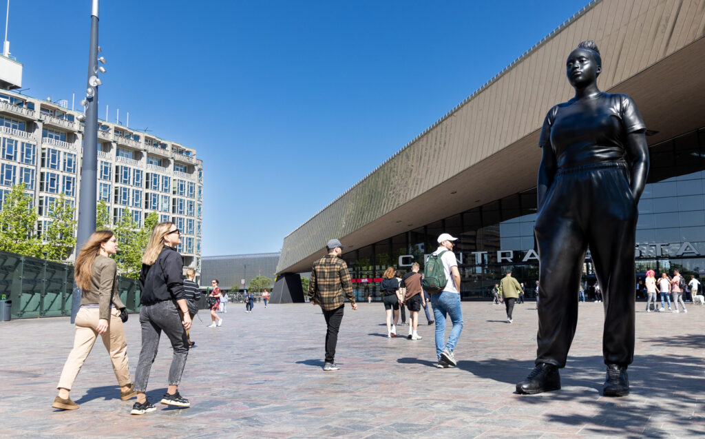 Moments Contained, het bijna 4 meter hoge bronzen beeld van een jonge, fictieve, gekleurde vrouw op sneakers, handen gebald in de zakken van haar trainingspak. Met een uitstraling van weerbaarheid, zelfvertrouwen en kwetsbaarheid. Het beeld staat op het Stationsplein, direct voor het Centraal Station.  De vrouw staat niet op een sokkel, maar met beide voeten op de grond. Het beeld is gemaakt door de Engelse kunstenaar Thomas J Price en is aan de stad Rotterdam geschonken door de Stichting Droom en Daad. Het maakt deel uit van de Internationale Beelden Collectie van Rotterdam. Het beeld werd begin juni 2023 onthuld. Op de foto zien we goed hoe groot het beeld is door de mensen die er omheen lopen.
