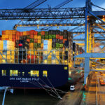 Schip in de containerterminal waar containers op en af het schip geladen worden door de kranen in de avond.