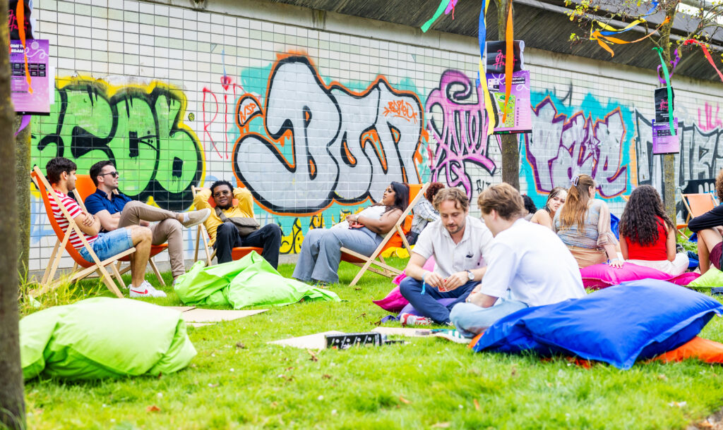 Festival in Rotterdam waar jongeren op zitzakken, klapstoeltjes en in het gras zitten met graffiti op de muren.