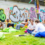 Festival in Rotterdam waar jongeren op zitzakken, klapstoeltjes en in het gras zitten met graffiti op de muren.