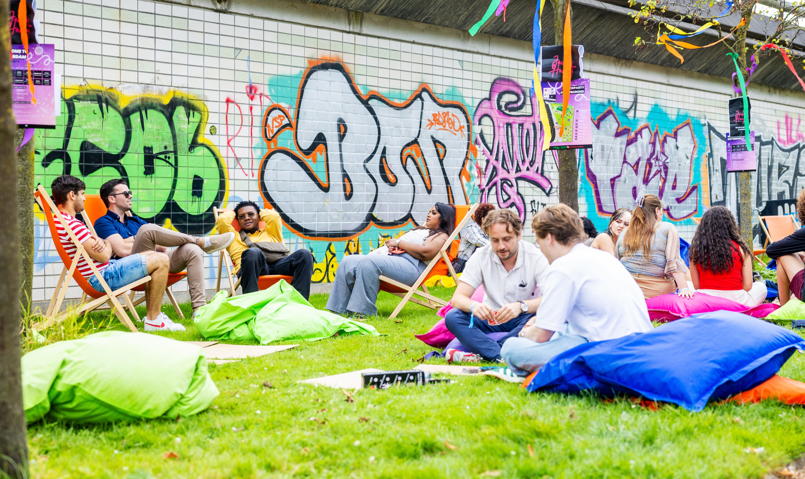 Festival in Rotterdam waar jongeren op zitzakken, klapstoeltjes en in het gras zitten met graffiti op de muren.